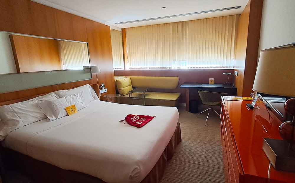 My room at Hotel Alfonso, with a large bed in the centre and retro styled furniture in orange and green surrounding it. There is a large window on one wall.