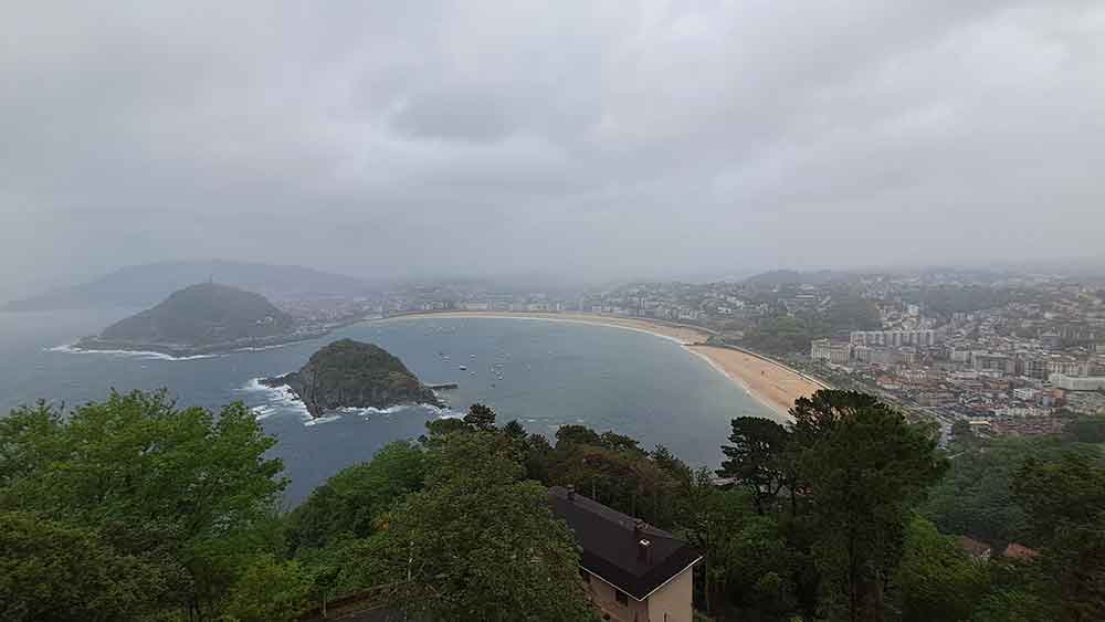 Monte Igeldo looking down on Concha Bay in the rain with grey clouds covering the landscape. 