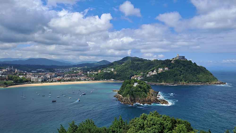 Concha Bay with a slim sndy beach and a rockyisland surrounded by more hills with greenery. 