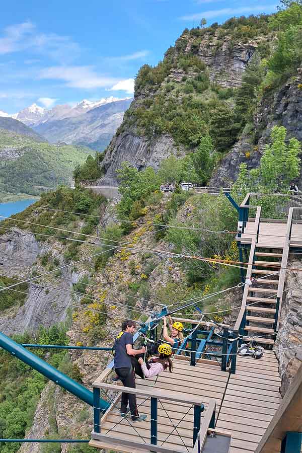Two people, one is Bella from our group, on a wooden platform overlooking the lake and mountians in the background. They are getting strapped into the Big Swing.
