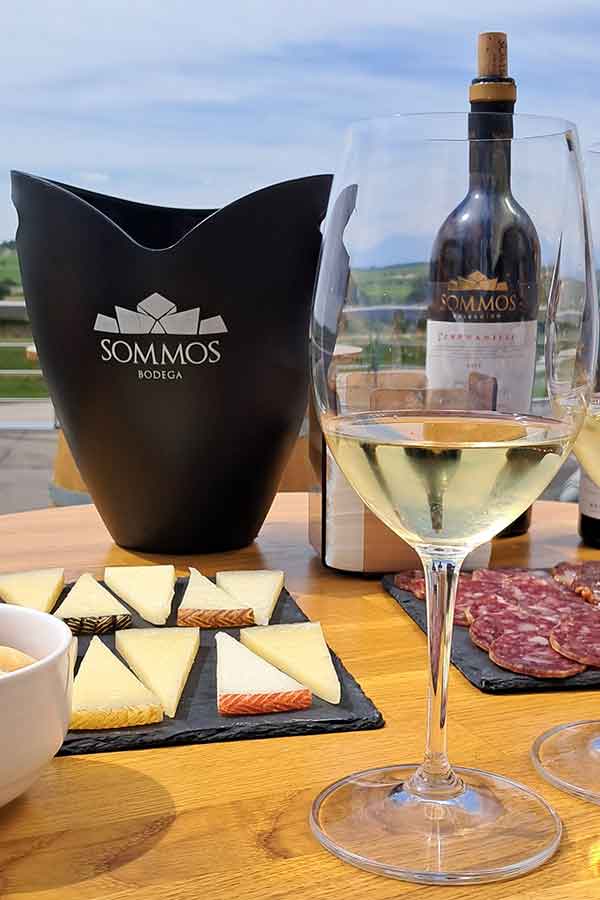 An Epic 5 Days Road Trip in Aragón Itinerary 26 A table with a bottle of Sommos wine and a wine cooler in thebackground. There is a platter of cured meats and cheeses on the table with a glass of white wine in the forground.
