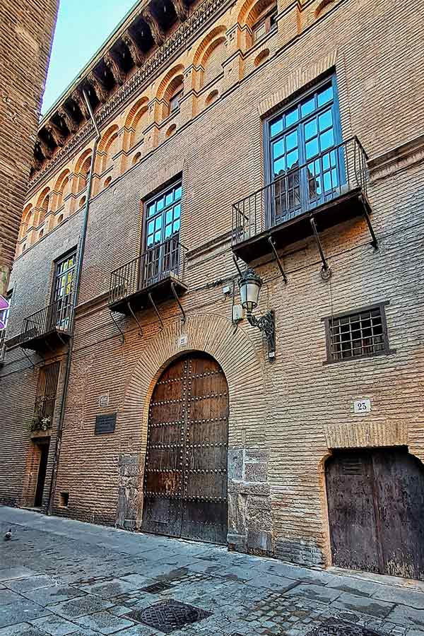 An old building in the historic cenntre of Zaragoza with an arch shaped wooden door and windows with balconies above.