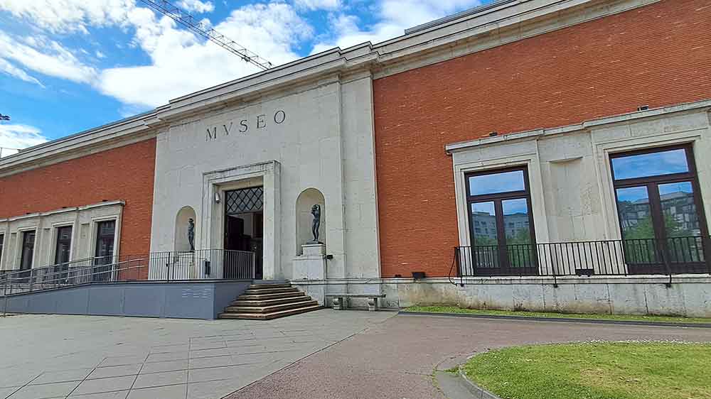 The entrance of Bilbao Fine Arts Museum with a red brick buildin and a light brick entranceway. There are steps and a ramp leading up.
