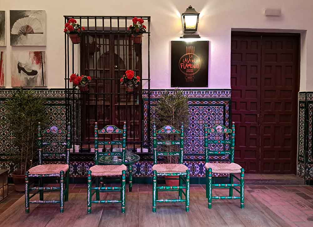four small green traditionally decorated chairs on a small stage at the intimate venue of La Casa del Flamenco in Seville