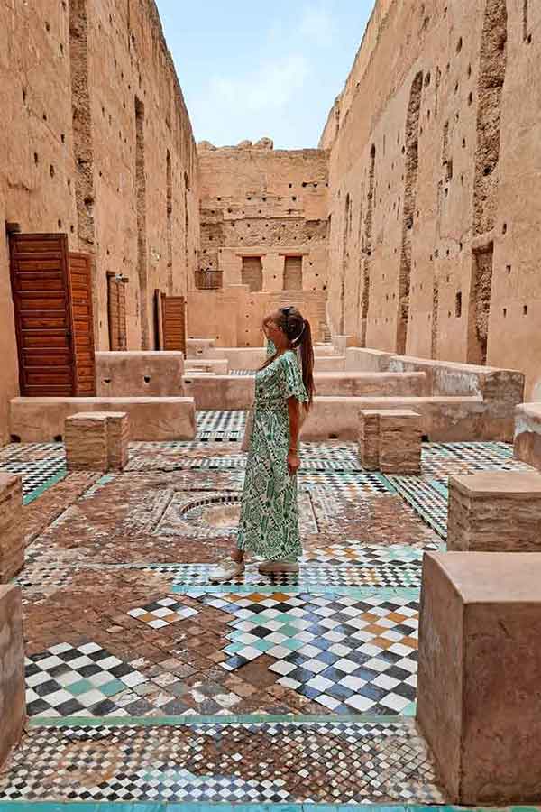 A woman (me) wearing a long pattered white and green dress. Stood on a mozaic floor in a ruin of a palace in Marrakech. This image is an example of what to wear in Marrakech (& Morocco) as a woman.