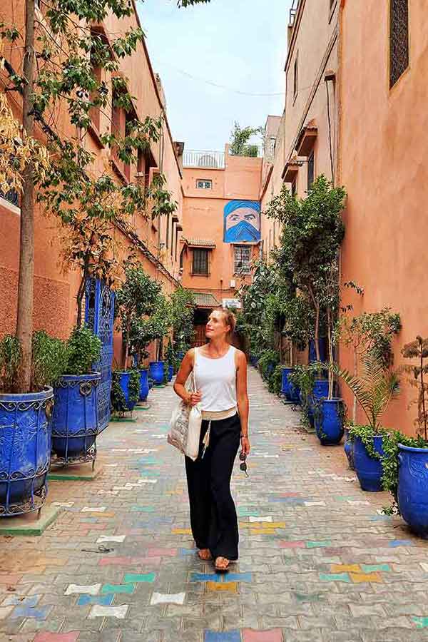 Me wearing a white sleeveless top and black floaty pants walking on the street of Marrakech. Make sure you add a pair of floaty harem pants to your Morocco packing list.