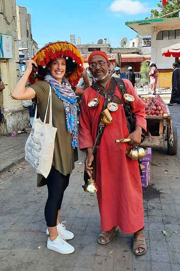 A woman (me) wearing a large brown blouse paired with leggings is taking a picture with a water man in Casablanca. Wondering what to wear in Morocco - this outfit was perfect.