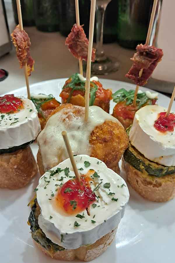 A plate of pintxos with various cheeses, breads, croquette all with sticks in them.