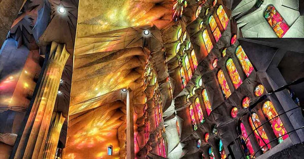 Stained glass windows inside La Sagrada Familia in Barcelona. The windows are shades of orange , yellow and red and they cast colouful shadows on the walls and columns. Barcelona is the starting city in this two week Spain and Portugal itinerary. I recommend visiting La Sagrada Familia during your time in Barcelona. 
