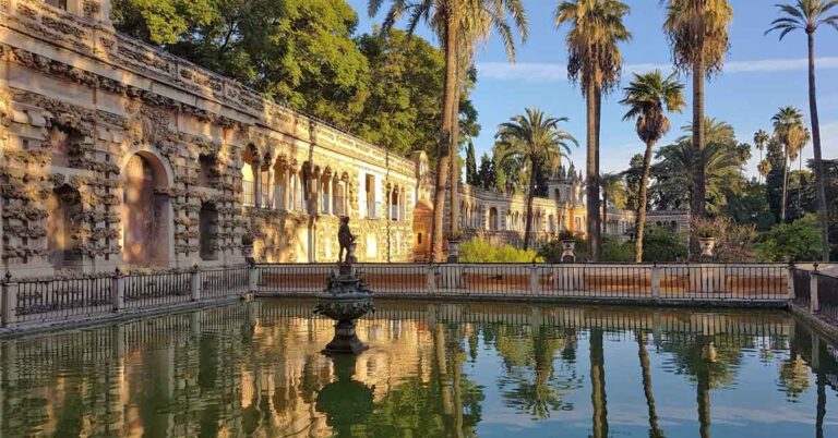 The gardens of the Royal Alcazar with a large pond surrounded by trees and walls. This is the featured image for 10 days in Spain itinerary. One of the destinations is Seville where you can see the Royal Alcazar and gardens.
