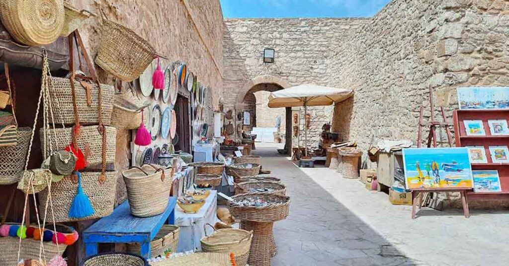A street in Essaouira, Morocco. This is an old sea wall with arches in it. Inisde the arches there are shops selling paitings, woven baskets and bags. Visit the city during this self-guided 10 days in Morocco itinerary.