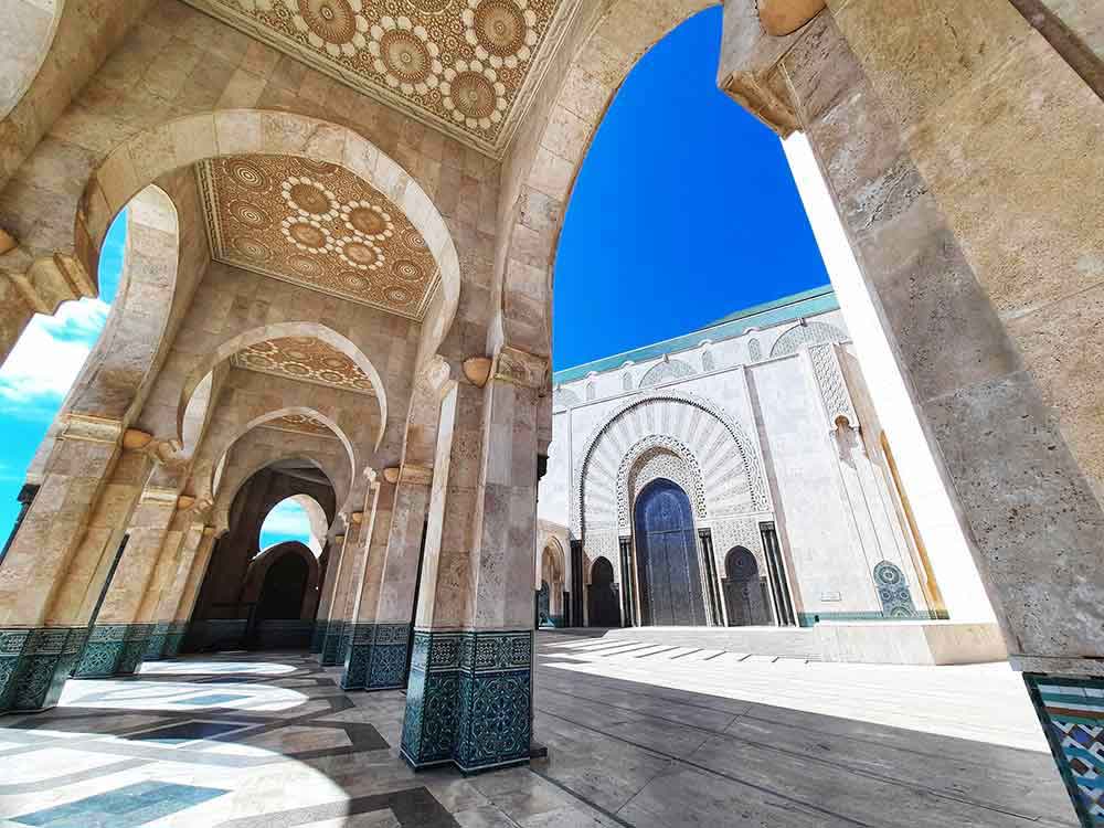 A view looking though the arched walkway at the Hassan II mosque in Casablanca. The sky is blue and the building is a light grey. self-guided 10 days Morocco itinerary from Casablanca to Marrakech