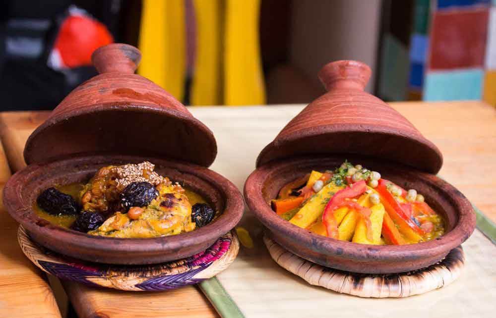 Two clay tagines are open, revealing delicious traditional meals of Marrakech. One features a meat dish with prunes, while the other is a vegetable dish, offering a balance of nutritious and hearty flavors.