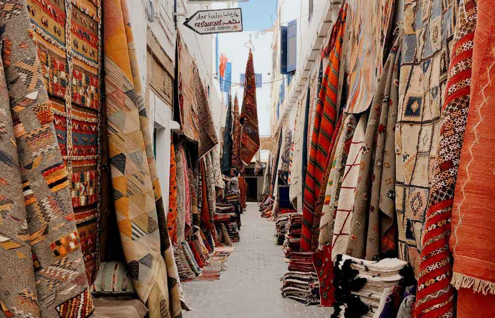 If you're wondering what to buy in Morocco, traditional Moroccan rugs and carpets are a great option. Colourful rugs hung up int he street. 