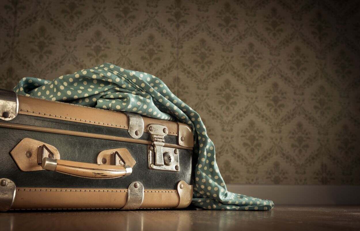 A brown vintage suitcase with brass buckles and a green spotted scarf.