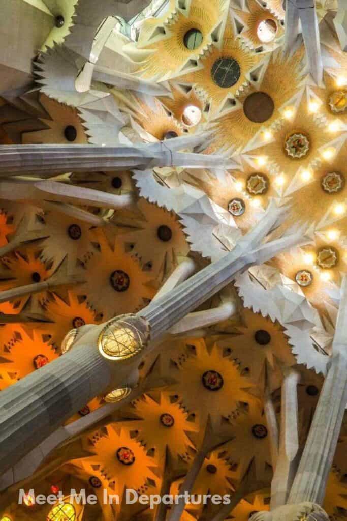 Sagrada Familia Stunning ceiling of the Sagrada Família in Barcelona, designed by Antoni Gaudí, with starburst-shaped patterns, towering columns branching like trees, and glowing warm-toned lights.