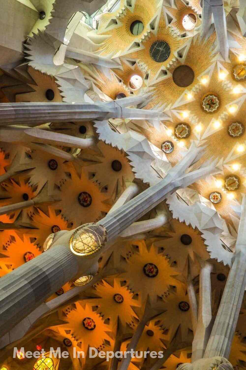 Stunning ceiling of the Sagrada Família in Barcelona, designed by Antoni Gaudí, with starburst-shaped patterns, towering columns branching like trees, and glowing warm-toned lights.