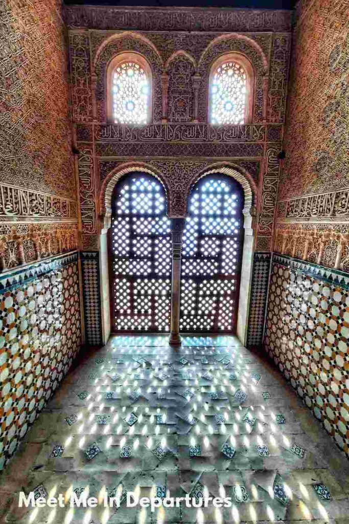Alhambra, Granada Intricate Moorish architecture inside the Alhambra, featuring geometric tile patterns on the walls and floors, with sunlight streaming through ornate lattice windows casting patterned light on the ground.