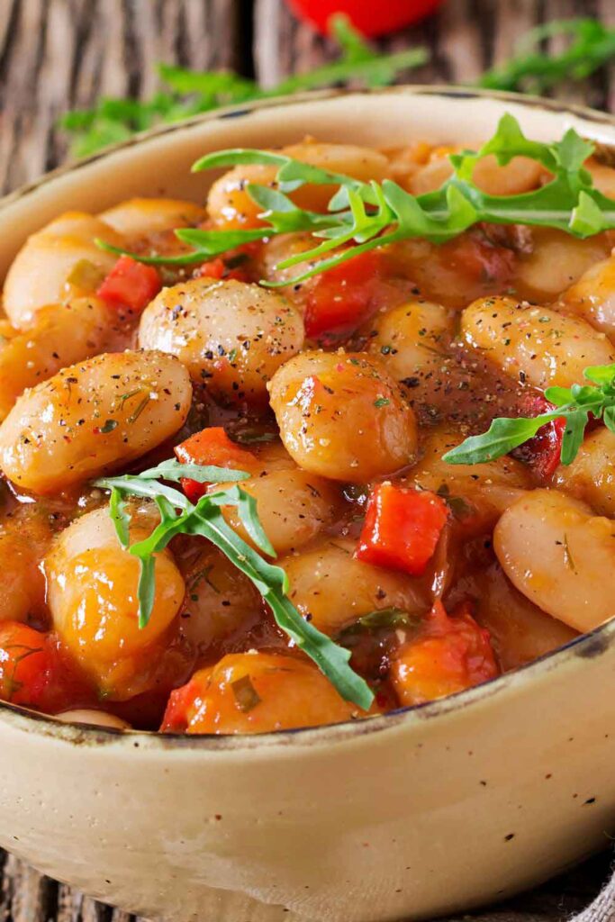 Close-up of a rustic Spanish stew made with large butter beans, red peppers, and fresh herbs. A hearty plant-based dish typical of Spanish home cooking.