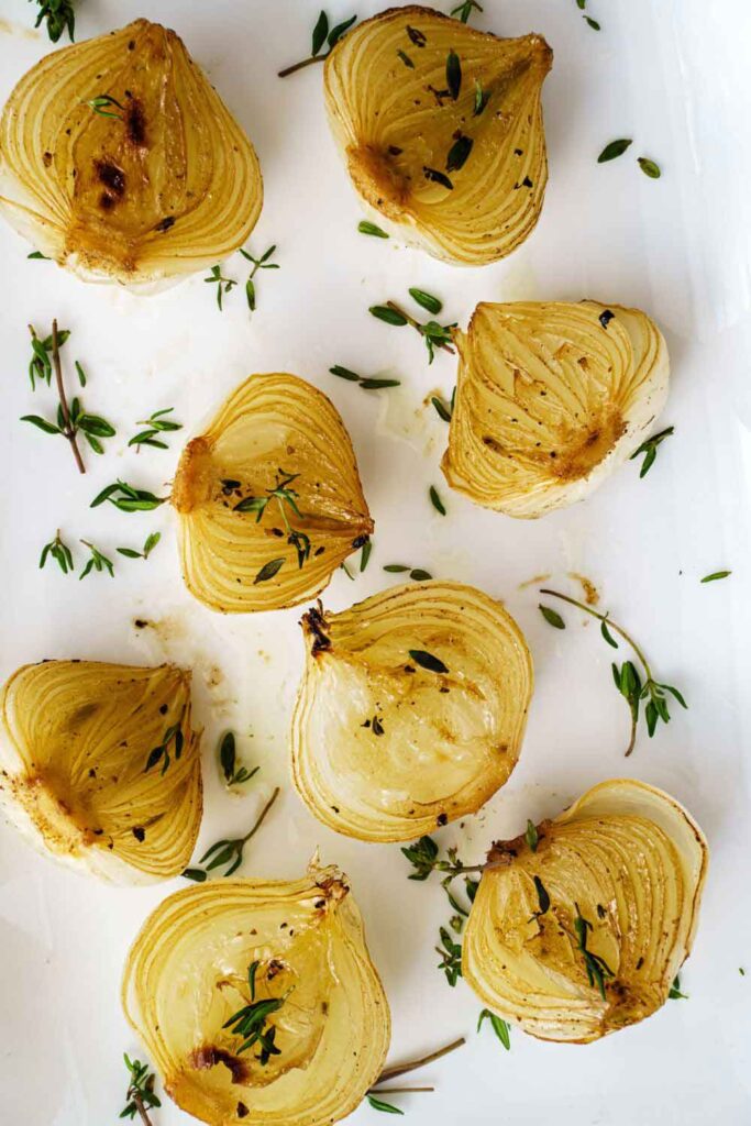 Golden roasted onion halves scattered with fresh thyme leaves. A simple side dish rooted in the earthy cooking traditions of Spain’s vegetable-based cuisine.
