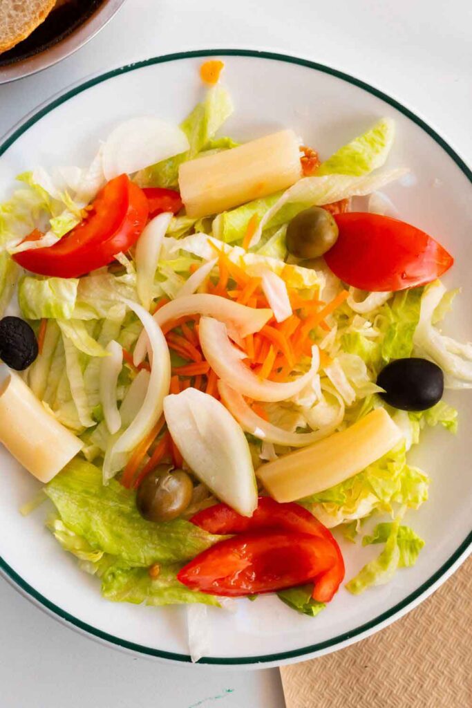 Plate of mixed greens topped with tomato wedges, olives, palm hearts, onions, and shredded carrots. A light starter often included in vegetarian-friendly menus across Spain.