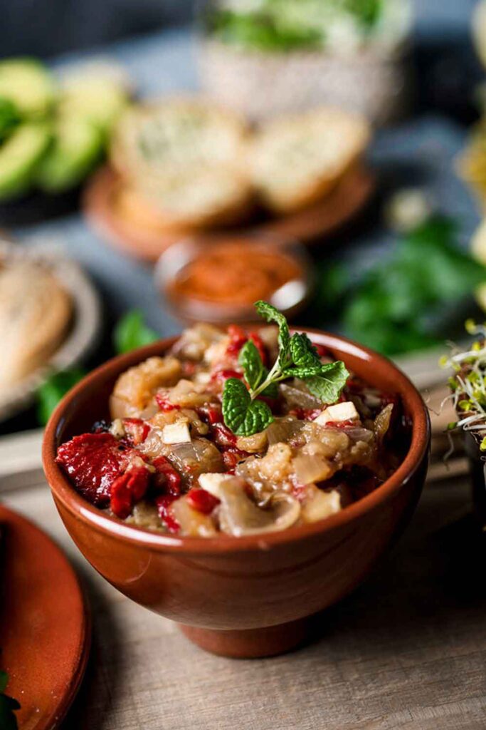 Clay bowl filled with roasted eggplant, red peppers, and onions topped with fresh mint. A Catalan specialty that’s a cornerstone of vegetable-focused cooking in Spain.