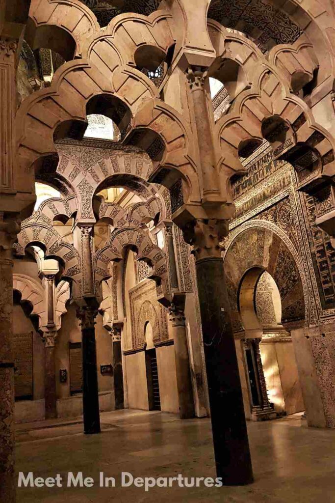 Interior of the Mezquita-Catedral in Córdoba showcasing a forest of intricately carved horseshoe arches, Moorish geometric patterns, and richly detailed stonework in warm lighting.
