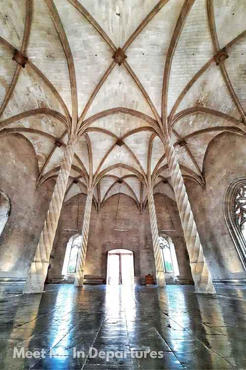 La Lonja, Palma de Mallorca Interior of the La Lonja, Palma de Mallorca, Spain, featuring a vaulted Gothic ceiling with intricately twisted stone columns rising from a reflective stone floor. The natural light from arched windows enhances the grandeur and symmetry of the historic space.