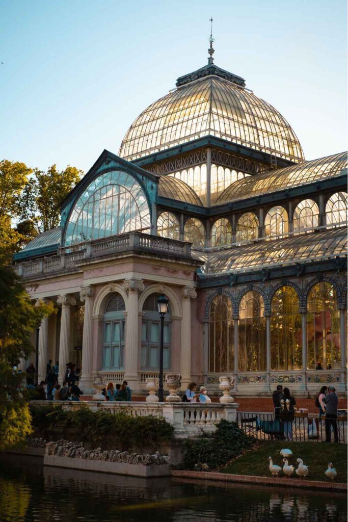 The Crystal Palace in El Retiro Park, Madrid, with people relaxing by the pond—an iconic landmark in one of the best cities to visit in Spain.