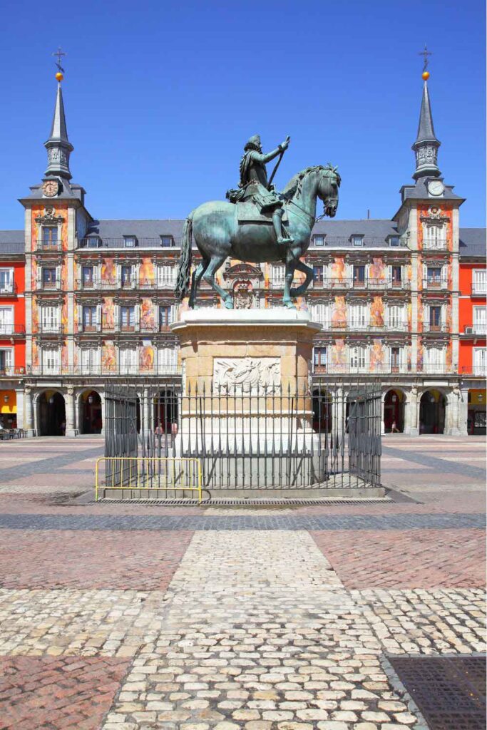 Statue of King Philip III on horseback in the centre of Plaza Mayor, one of the best things to do in Madrid, with the colourful façade of the surrounding buildings under a bright blue sky.