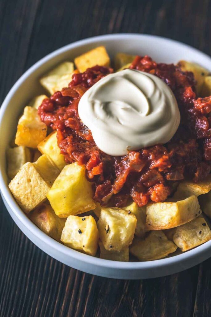 Bowl of crispy fried potatoes topped with spicy tomato sauce and aioli. A staple Spanish tapa that happens to be meatless and full of flavor.