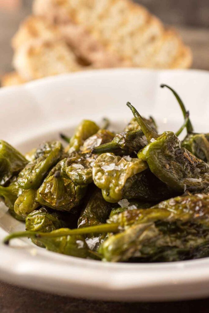 Plate of padrón peppers sprinkled with sea salt, served with bread in the background. A popular vegetarian tapa known for its occasional heat.