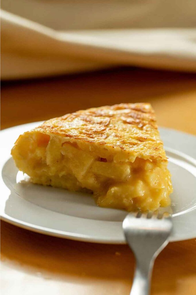Close-up of a golden slice of Spanish tortilla made with eggs and potatoes, served on a white plate. A classic meat-free option often found in Spanish cuisine.