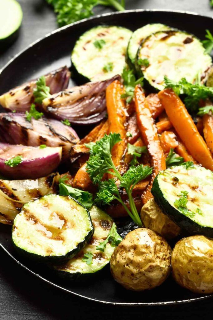 A colorful assortment of grilled vegetables including zucchini, carrots, red onions, and baby potatoes, garnished with parsley. This dish highlights the plant-forward traditions of Spanish cooking.