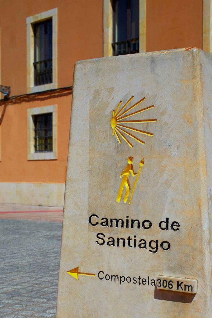 Signpost to Santiago de Compostela on the Camino trail Stone marker for the Camino de Santiago with a yellow scallop shell symbol and a hiker icon, indicating 306 km to Santiago de Compostela.