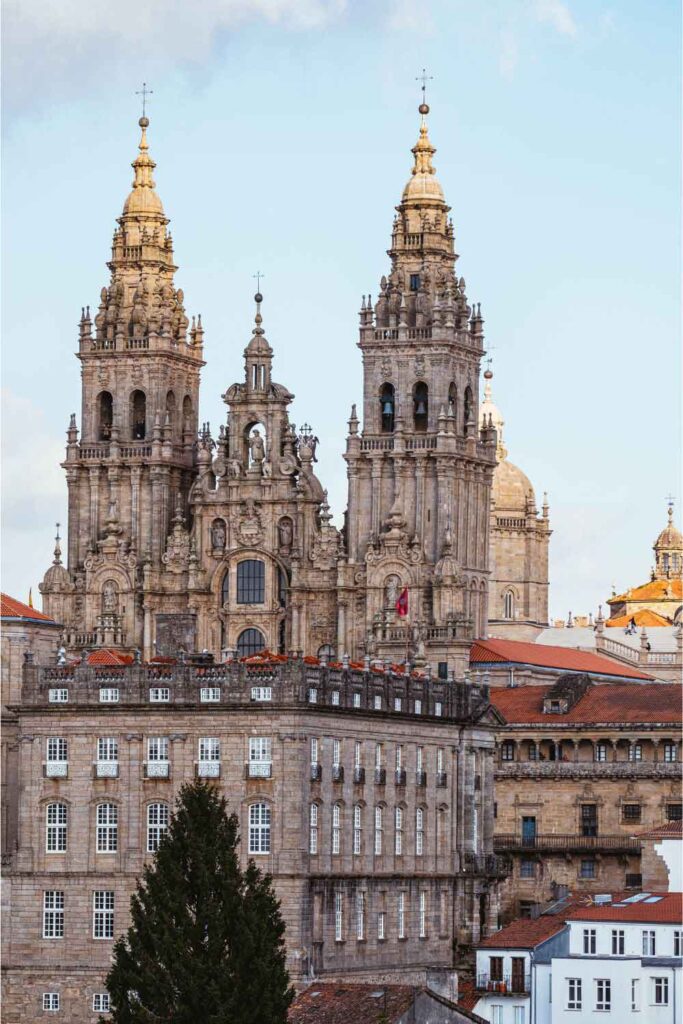 Cathedral at Santiago de Compostela Ornate twin-towered façade of the Cathedral of Santiago de Compostela, rising above historic stone buildings under a pale blue sky.