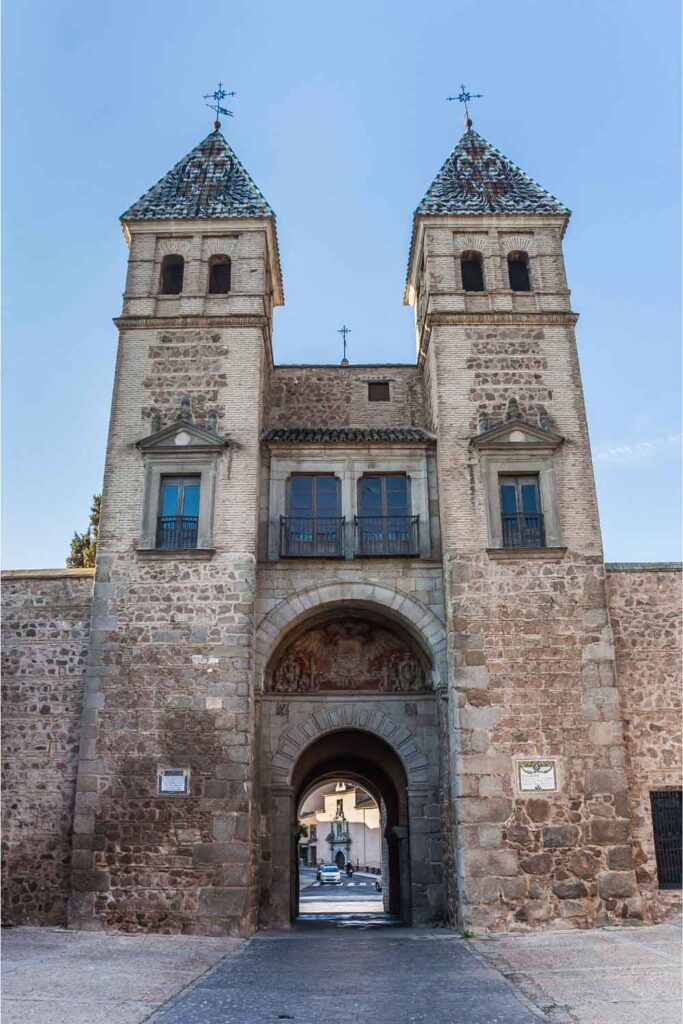 City Gate in Toledo Historic stone gateway with twin towers in Toledo, featuring arched entrances, decorative carvings, and a view through to the street beyond.