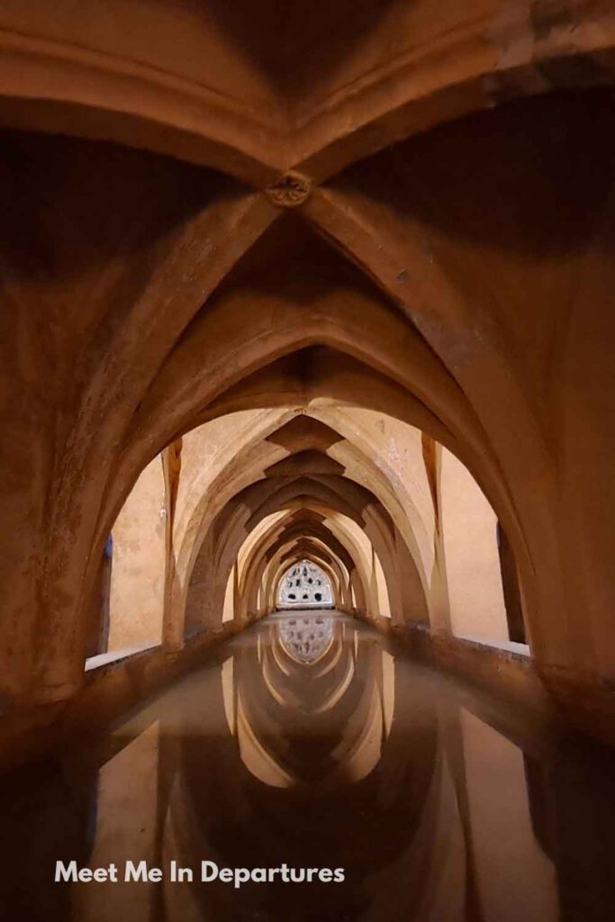 Arched vaulted ceiling reflected in the still waters of the Baños de Doña María de Padilla at the Real Alcázar of Seville, photographed during early morning access before the palace opened to the public.