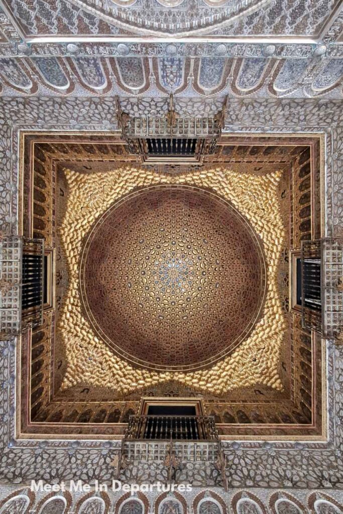 Upward view of the ornate gilded wooden dome ceiling in the Salón de los Embajadores at the Real Alcázar of Seville, displaying intricate geometric patterns, captured during early morning access before the palace opened to visitors.