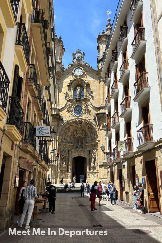People walking in Calle Mayor towards the ornate Baroque facade of the Basilica of Saint Mary of the Chorus in San Sebastian’s Old Town, one of the top things do in San Sebastian for history lovers.