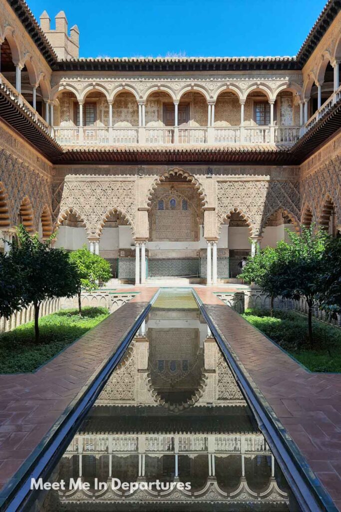 Ornate arches and intricate plasterwork reflected in the long central pool of the Patio de las Doncellas at the Real Alcazar of Seville, captured during a peaceful early-entry visit before the palace opened to the public.