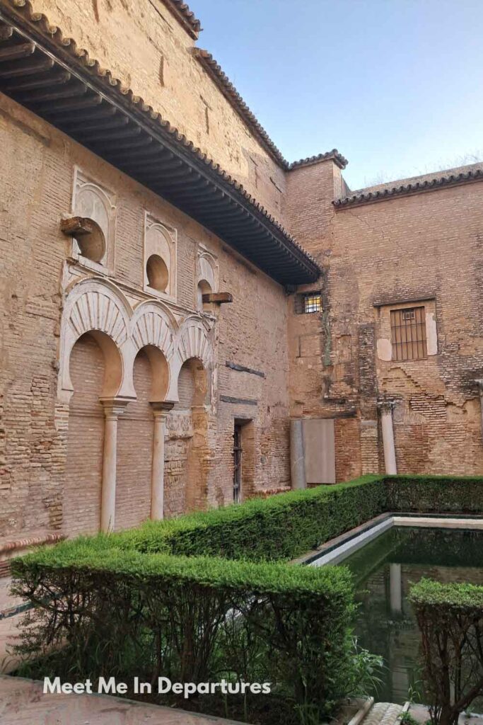 Patio del Yeso at the Real Alcázar of Seville, with Moorish arches, weathered brick walls, and a rectangular reflecting pool, photographed during early morning access before other visitors arrived.