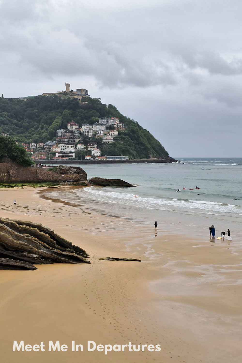 Zurriola Beach in San Sebastian with surfers in the water and Mount Urgull in the background, a favorite seaside destination in northern Spain.