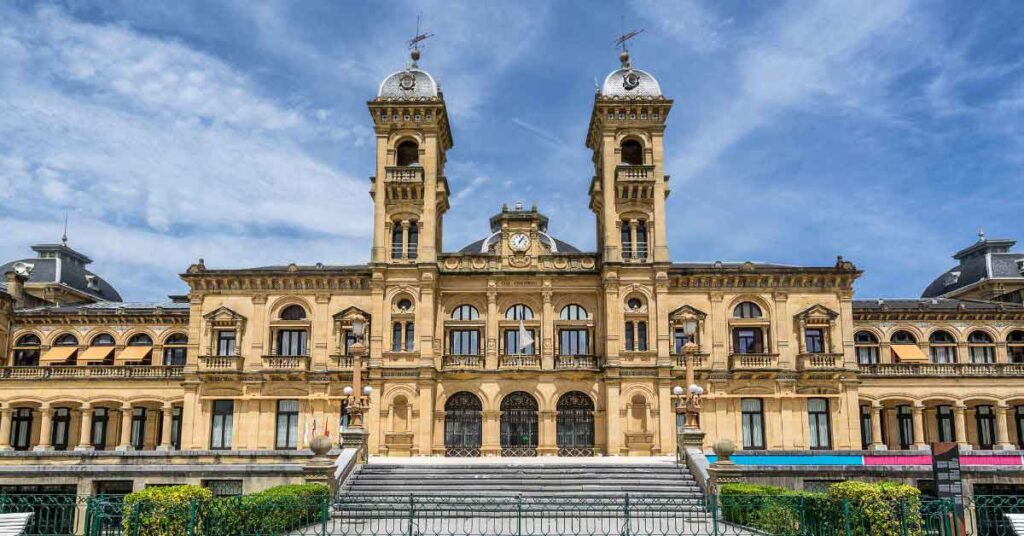 San Sebastian Town Hall, a grand sandstone building with twin clock towers and intricate balconies, set against a blue sky in northern Spain’s Basque Country, often highlighted among the top things to do in San Sebastian for its historic and cultural significance.