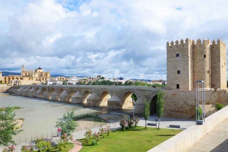 Roman Bridge and Temple, Córdoba View of the Roman bridge in Córdoba, one of the most striking ancient ruins in Spain, with the Calahorra Tower and Mosque-Cathedral visible in the background under a cloudy sky.