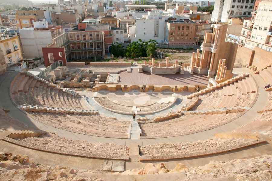 The Roman theatre in Cartagena, Spain, with semi-circular stone seating and surrounding cityscape.