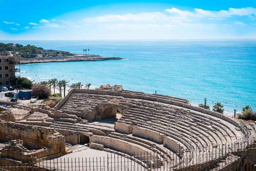 The seaside Roman amphitheatre in Tarragona, Spain, with stone seating and the Mediterranean Sea in the background.