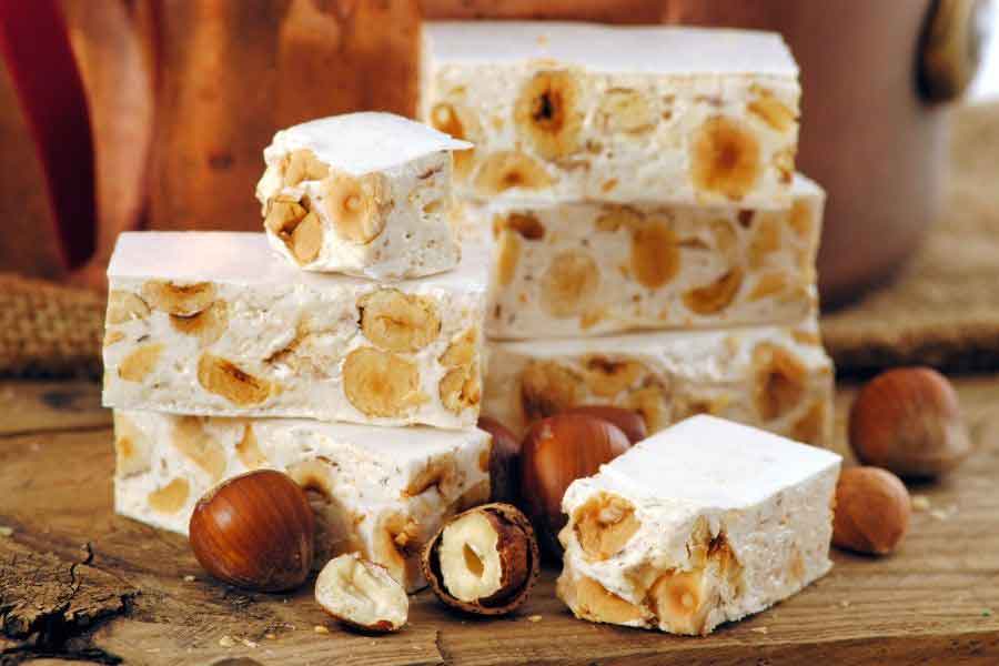 Blocks of traditional Spanish turrón filled with toasted nuts, placed on a wooden board — a sweet and festive treat often bought as a souvenir from Spain.