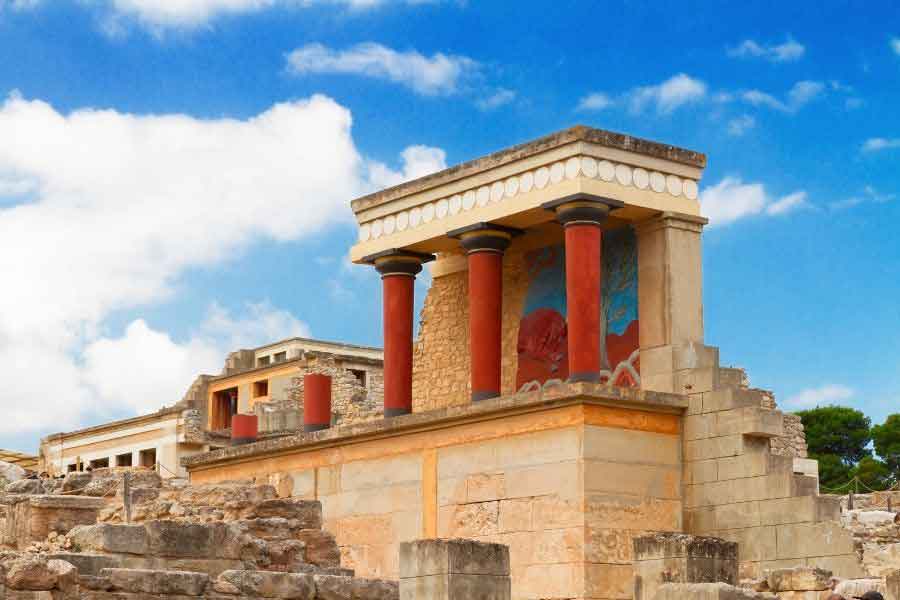 Knossos Ruins, Crete The restored section of the Palace of Knossos in Crete, featuring vivid red Minoan columns and a colourful fresco beneath a bright blue sky. The site’s sunlit stone ruins are a striking reminder of ancient civilisations and a popular stop for those seeking warm winter days in southern Europe.