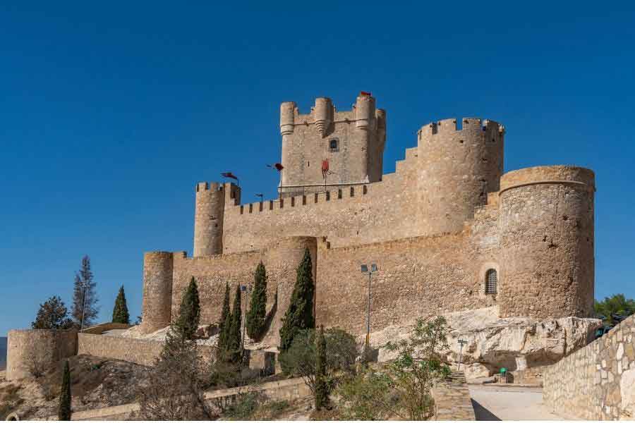 Castillo de Belmonte in Castilla-La Mancha, a well-preserved medieval fortress with round towers and crenellated walls, set against a clear blue sky.